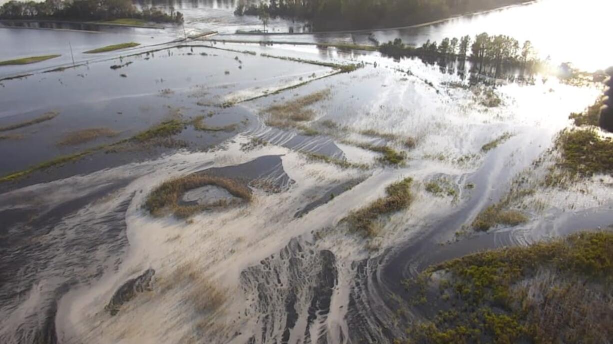 FILE - In this file image made from Sept. 21, 2018 drone video provided by the N.C. Department of Environmental Quality, light gray material flows out of a flooded coal ash dump toward the Cape Fear River at Duke Energy’s L.V. Sutton Power Station near Wilmington, N.C. Duke Energy said Wednesday, Sept. 4, 2019, that it had completed extensive repairs to the dam that breached during Florence at the L.V. Sutton Power Station. (N.C.