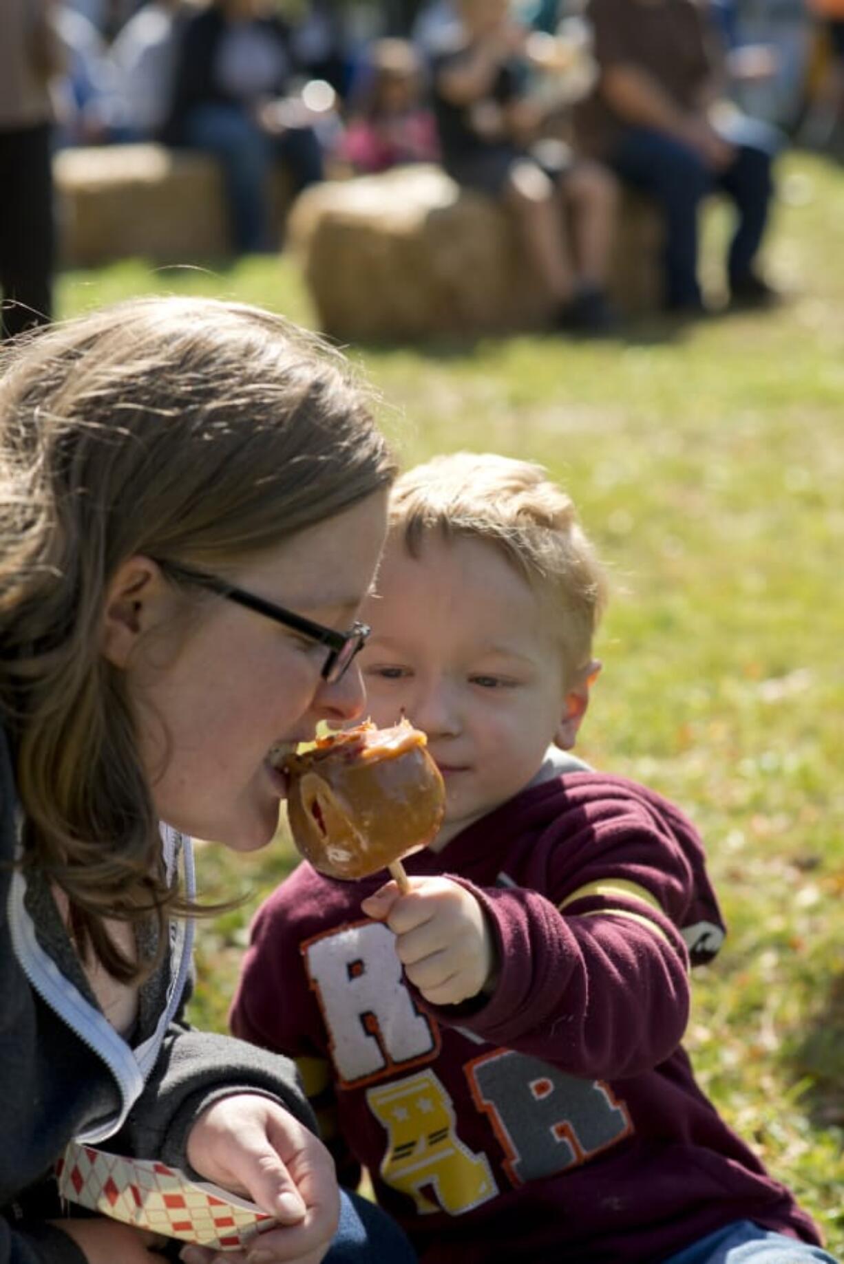 Jessica Peters takes a bite of a caramel apple offered by her 4-year-old son, Calvin, during Saturday&#039;s Old Apple Tree Festival at Vancouver&#039;s Old Apple Tree Park.