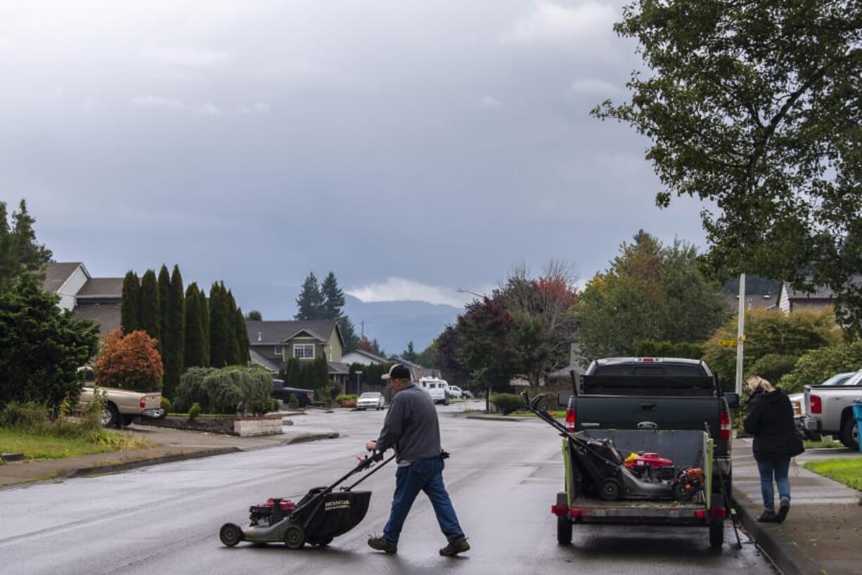 Charlie White with Thomason Landscaping Company pushes a lawn mower across a street while woking on yards in Orchards on Thursday afternoon, Oct. 3, 2019.