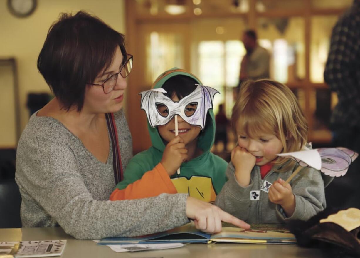 Max Hoskins, 5, center, shows off his bat mask while reading a book with Rowena Hoskins, left, and Opal Hoskins, 3, right. The Hoskins were among the attendees at the Vancouver Water Resources Education Center's "Creatures of the Night" event on Saturday.