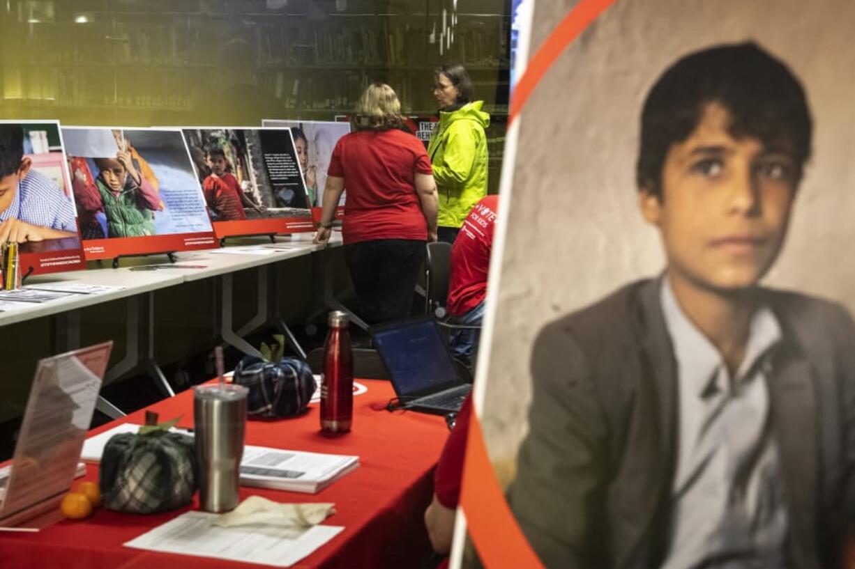 Stephanie Wick, a volunteer with the Save the Children Action Network, left, speaks to Lori Hume of Vancouver during a Save the Children photo gallery event Wednesday night at the Vancouver Community Library. The organization brought a series of photos featuring refugee children to the library as part of its Stop the War on Children Week of Action. The photos will be on display until Oct. 23.