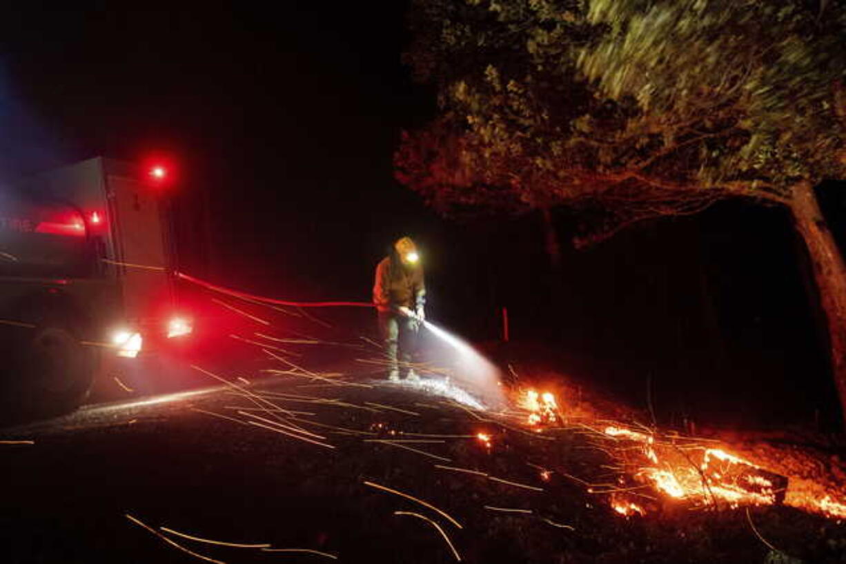 A firefighter battling the Kincade fire extinguishes a hot spot as strong winds send embers flying in Calistoga, Calif., on Tuesday, Oct. 29, 2019. Millions of people have been without power for days as fire crews raced to contain two major wind-whipped blazes that have destroyed dozens of homes at both ends of the state: in Sonoma County wine country and in the hills of Los Angeles.