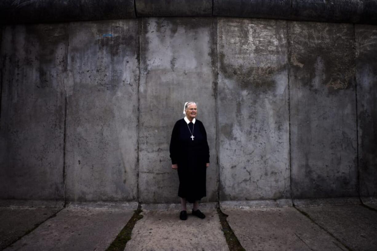 In this Sept. 18, 2019, photo, Sister Brigitte Queisser of the Lutheran Lazarus Order poses for a photo in front of concrete remains of the Berlin Wall during an interview with The Associated Press in Berlin. For many years, Sister Brigitte and other deaconesses lived in West Berlin across the street from the wall in the mother house of the Lutheran Lazarus Order, which ran a hospital where many of the people injured while escaping from East Berlin were treated.