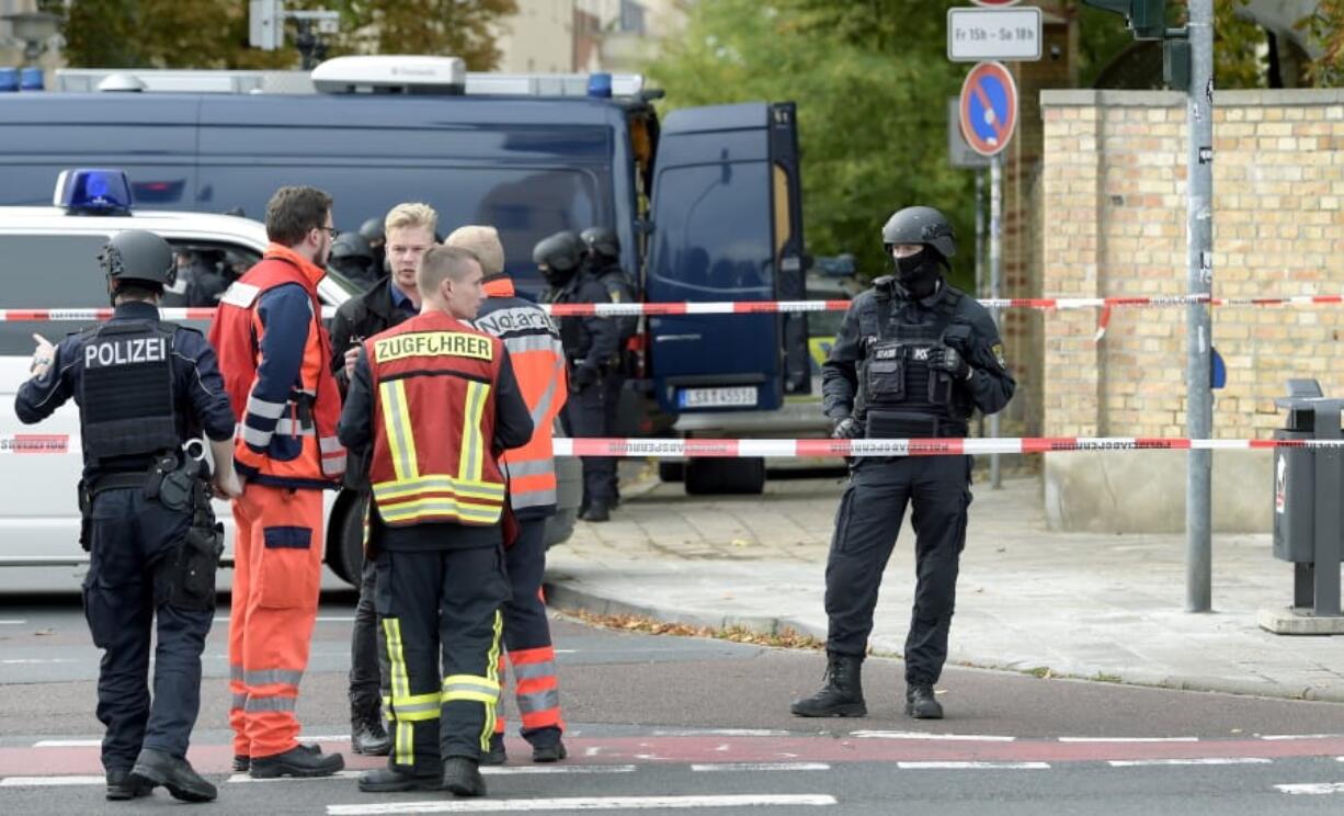 Police officers and paramedics stay in front of a Jewish cemetery in Halle, Germany, Wednesday, Oct. 9, 2019. One or more gunmen fired several shots on Wednesday in the German city of Halle. Police say a person has been arrested after a shooting that left two people dead.