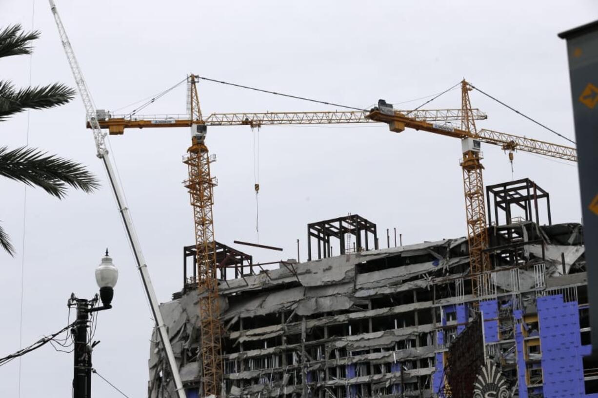 Two unstable cranes loom over the construction of a Hard Rock Hotel, Thursday, Oct. 17, 2019, in New Orleans.  The 18-story hotel project that was under construction collapsed last Saturday, killing three workers. Two bodies remain in the wreckage. Authorities say explosives will be strategically placed on the two unstable construction cranes in hopes of bringing them down with a series of small controlled blasts ahead of approaching tropical weather.