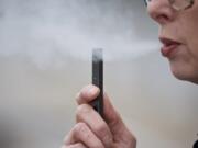 FILE - In this April 16, 2019, file photo, a woman exhales a puff of vapor from a Juul pen in Vancouver, Wash. A former Juul Labs executive is alleging that the vaping company knowingly shipped 1 million tainted nicotine pods to customers. The allegation comes in a lawsuit filed Tuesday, Oct. 29, by a former finance executive who was fired by the vaping giant earlier this year.