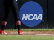 FILE - In this April 19, 2019, file photo, an athlete stands near a NCAA logo during a softball game in Beaumont, Texas. The NCAA is poised to take a significant step toward allowing college athletes to earn money without violating amateurism rules. The Board of Governors will be briefed Tuesday, Oct. 29 by administrators who have been examining whether it would be feasible to allow college athletes to profit of their names, images and likenesses. A California law set to take effect in 2023 would make it illegal for NCAA schools in the state to prevent athletes from signing personal endorsement deals. (AP Photo/Aaron M.