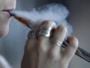 A woman using an electronic cigarette exhales a puff of smoke.