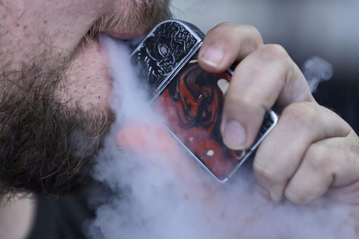 FILE - In this Friday, Oct. 4, 2019 photo, a man using an electronic cigarette exhales in Mayfield Heights, Ohio. Vaping-related illnesses in the U.S. are still rising, though at a slightly slower pace. On Thursday, Oct. 17, 2019, the Centers for Disease Control and Prevention said there have been nearly 1,500 cases and at least 33 deaths in the still mysterious outbreak.