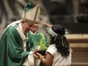 An Amazon indigenous girl gives Pope Francis a plant Sunday during the offertory of a Mass for the closing of Amazon synod in St. Peter&#039;s Basilica at the Vatican.