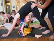 Saffron Smith, 2, looks up while yoga teacher Daniele Strawmyre helps her mother, Jennifer Smith, with a downward dog pose during a Ready Set Grow yoga class at the Slocum House in Esther Short Park on Saturday, October 26, 2019. Ready Set Grow is a yoga studio based in Portland and Vancouver.