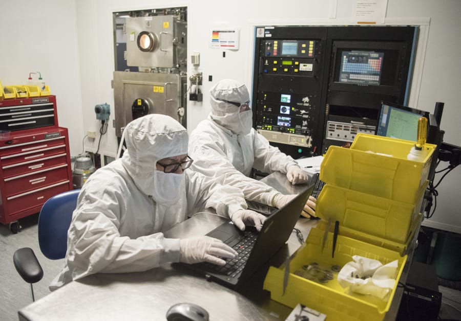 nLIGHT technicians Carlito Gutierrez, left, and Stefan Ilchenko work from computers near an optical coding machine, pictured back left, which spins strips of lasers, in the nLIGHT lab in Vancouver.