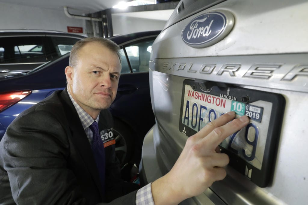 Tim Eyman, a career anti-tax initiative promoter, poses for a photo with the expired car registration tabs on his SUV, Tuesday, Nov. 26, 2019, in a parking garage in Seattle.(AP Photo/Ted S.