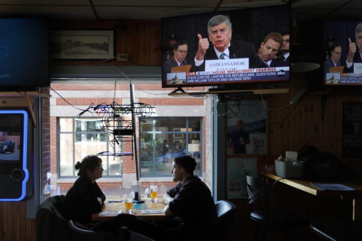 Olivia Tobin and her fiance, Jordan Ashby, ignore the televised impeachment hearings playing on monitors at the Commercial Street Pub, Wednesday, Nov. 13, 2019, in Portland, Maine. Tobin is an Irish citizen who has a green card to live and work in the U.S. and said she only pays attention to the hearings if it seems likely that the Trump will be held accountable. (AP Photo/Robert F.