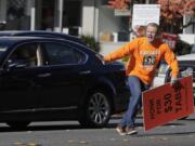 Anti-tax activist Tim Eyman darts across traffic after he stopped to shake hands with a motorist who honked at him as he waved a sign supporting Initiative 976, which would cut most car registration tabs to $30 in Washington state, Tuesday, Nov. 5, 2019, on election day in Bellevue, Wash. If passed by voters, the measure would leave state and local governments scrambling to pay for road paving and other transportation projects. (AP Photo/Ted S.