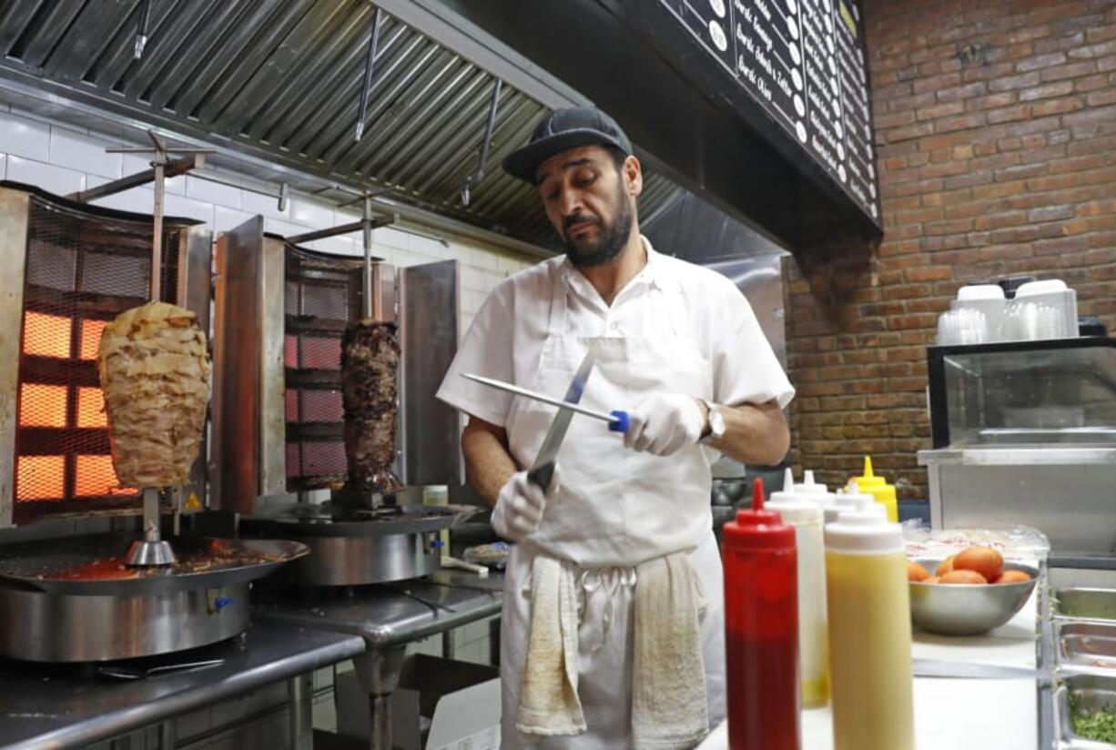 In this Wednesday, Oct. 9, 2019, photo, chef Diaa Alhanoun sharpens his knives between serving customers, while skewered pieces of cooked chicken and beef known, or &quot;shawarma,&quot; are kept warm at his restaurant Sakib, in New York. A Syrian refugee fleeing civil war at home, Alhanoun, his wife and four children arrived in the U.S. from Jordan in 2016. Less than three years later Alhanoun and a partner opened a small restaurant in Brooklyn&#039;s trendy Williamsburg neighborhood.