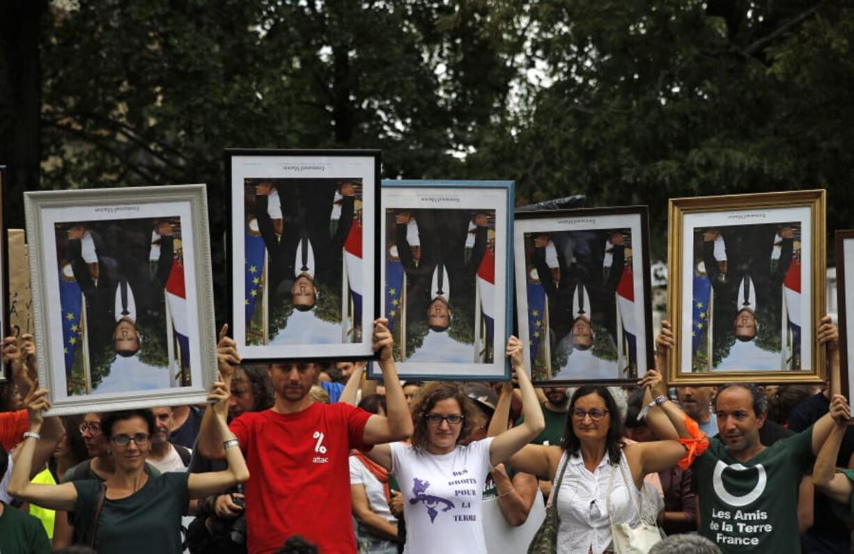 FILE - In this Aug. 25, 2019 file photo, demonstrators hold up upside down portraits of French President Emmanuel Macron during a protest in Bayonne, France. One by one, environmental activists around France have been taking portraits of President Emmanuel Macron down from scattered town halls this year. The portrait-removers, have been facing trials around the country, with some fined, others released. An appeals court in Lyon is reconsidering the first conviction handed down over portrait removal Tuesday.