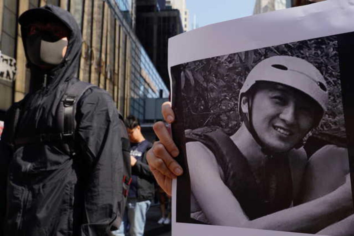 A protester stands near a photo of Chow Tsz-Lok during a memorial flash mob to remember him in Hong Kong on Friday, Nov. 8, 2019. Chow, a Hong Kong university student who fell off a parking garage after police fired tear gas during clashes with anti-government protesters died Friday, in a rare fatality after five months of unrest that intensified anger in the semi-autonomous Chinese territory.