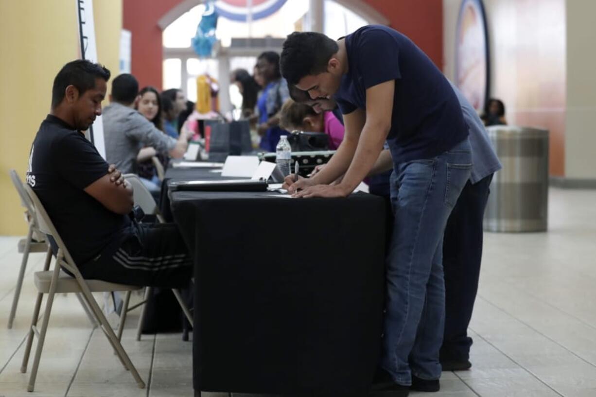 FILE - In this Oct. 1, 2019, file photo Billy Ramos, right, fills out a job application with Adidas during a job fair at Dolphin Mall in Miami. On Friday, Nov. 1, the U.S. government issues the October jobs report.