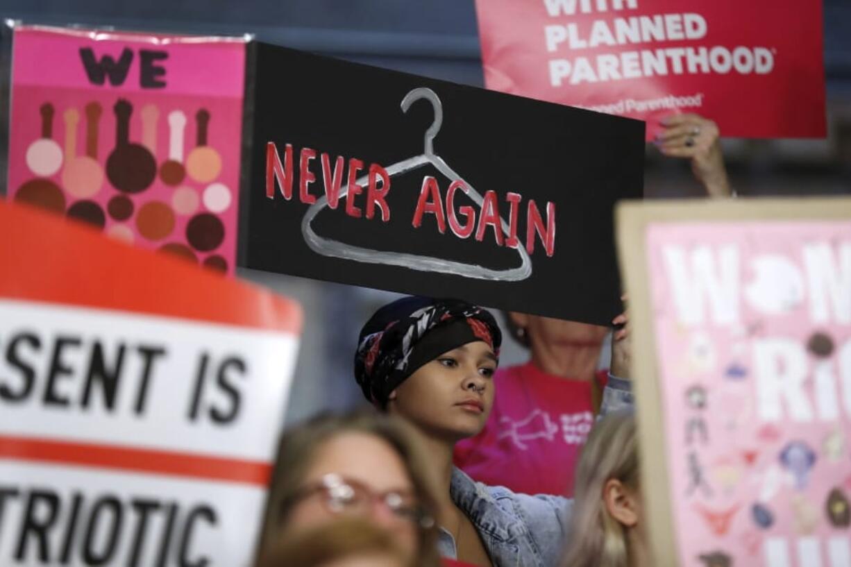 FILE - In this Tuesday, May 21, 2019 file photo, August Mulvihill, of Norwalk, Iowa, center, holds a sign depicting a wire clothes hanger during a rally at the Statehouse in Des Moines, Iowa, to protest recent abortion bans. On Wednesday, Nov. 6, 2019, a federal judge in New York struck down a rule letting health care clinicians object to providing abortions and other services on moral or religious grounds.