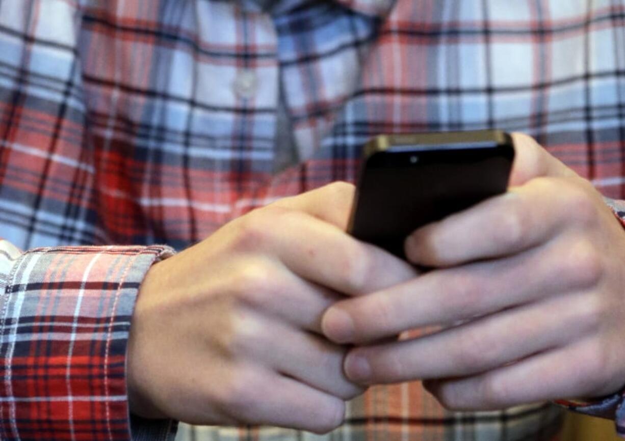 FILE - In this Oct. 24, 2013, file photo, a person checks their smartphone in Glenview, Ill. A mysterious wave of texts swept America&#039;s phones overnight Wednesday, Nov. 6, 2019, delivering unintelligible messages that left many people mildly confused when they woke up on Thursday. (AP Photo/Nam Y.