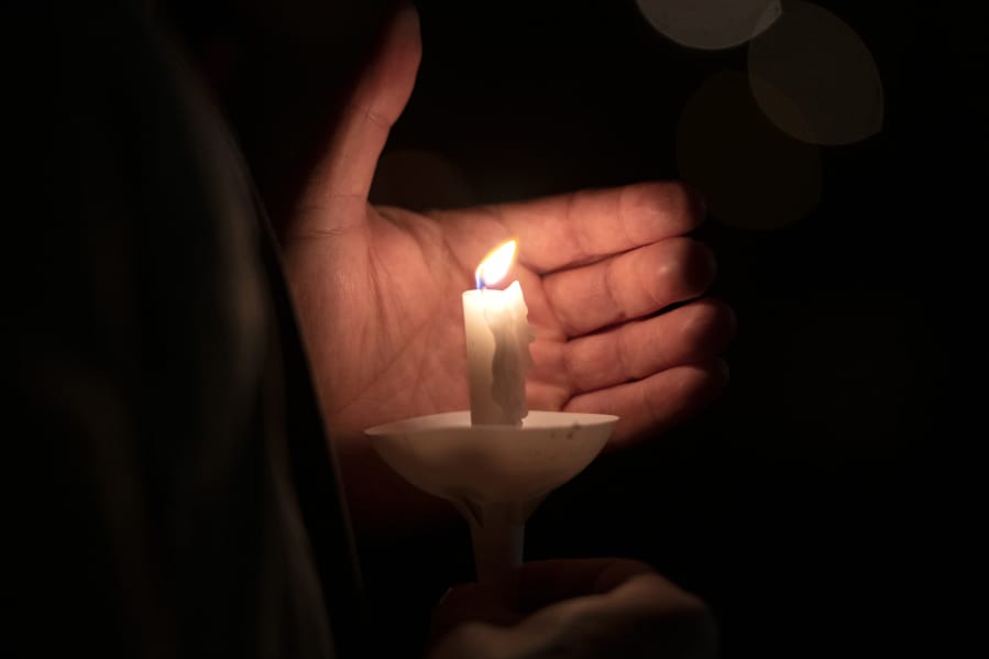 A vigil participant blocks the breeze to keep his candle lit in honor of Tiffany Hill on Sunday night at Esther Short Park in Vancouver.