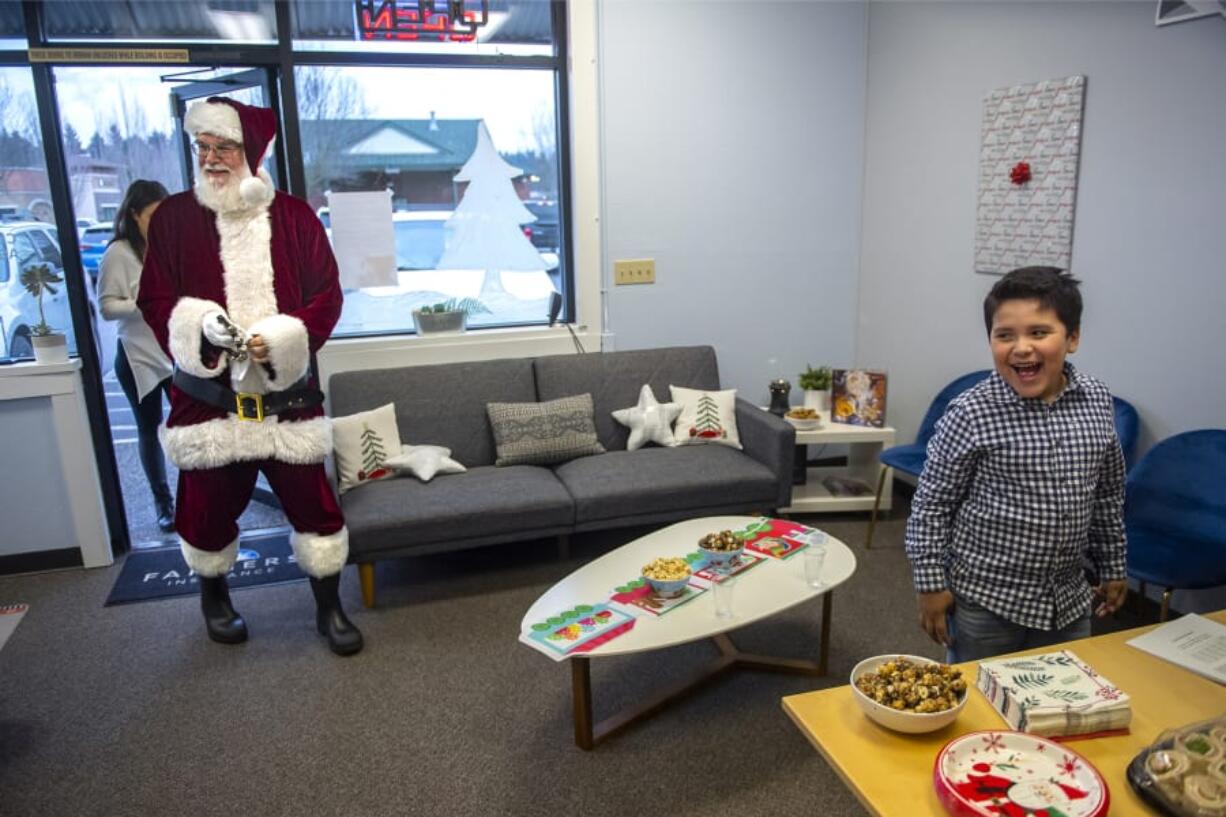 Santa Claus, played by Ted Mach of Battle Ground, walks into Farmers Insurance in Salmon Creek as Owen Sanchez-Jauregui, 7, reacts to seeing him Wednesday.