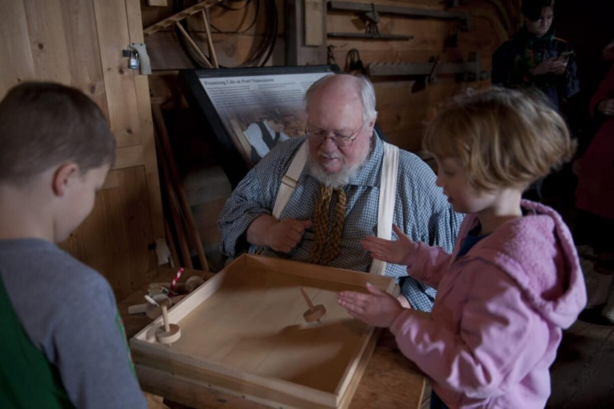 Volunteer Al Williams, center, offers tips for how to spin wood tops Saturday to Stephan Laabs, 7, left, and Iridium Jewel, 7, both of Vancouver.