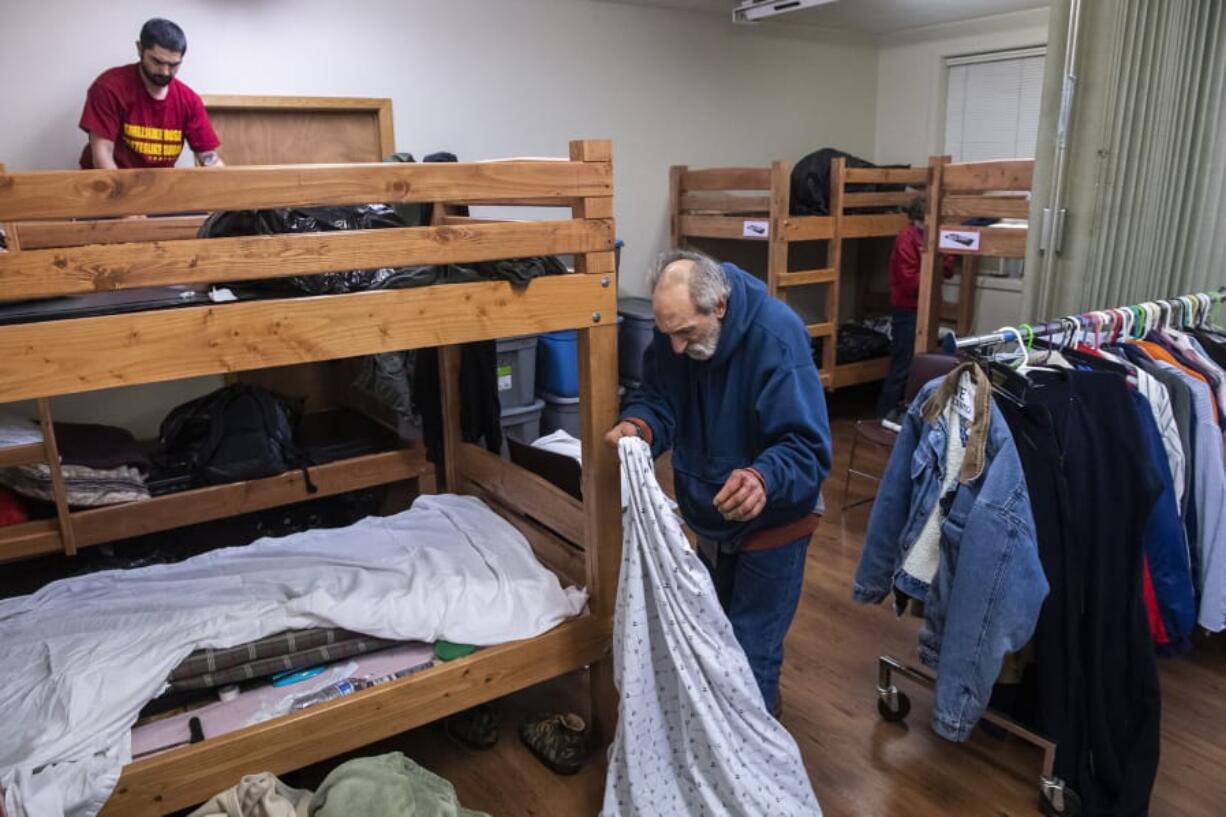 Tyler Taplin, left, and Chad Calhoun make their beds inside the Winter Hospitality Overflow shelter at St. Paul Lutheran Church in downtown Vancouver ahead of a chilly night on Monday. The Vancouver City Council will likely approve a grant that would increase funding to the shelter, allowing operators to keep it open year-round instead of just five months out of the year.