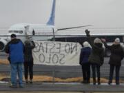 Activists in Yakima wave encouragement to a detainee in shackles boarding a U.S. Immigration and Customs Enforcement flight bound for Mesa, Arizona. ICE moved the flights to the Central Washington city in May after King County officials booted them from Boeing Field near Seattle, saying deportations raised troubling human rights concerns.