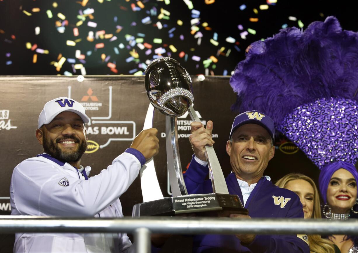 Jimmy Lake, left, Washington defensive coordinator and incoming head coach, and Washington head coach Chris Petersen pose with the Las Vegas Bowl trophy after they defeated Boise State in the Las Vegas Bowl NCAA college football game at Sam Boyd Stadium, Saturday, Dec. 21, 2019, in Las Vegas.