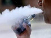 FILE - In this Aug. 28, 2019, file photo, a man exhales while smoking an e-cigarette in Portland, Maine. Health officials investigating a nationwide outbreak of vaping-related illnesses have, for the first time, listed the vape brands that are most commonly linked to hospitalizations. Most of the nearly 2,300 people who has suffered lung damage were vaping liquids that contain THC, the high-inducing part of marijuana. In a report released Friday, Dec. 6 the government listed the THC-containing products that patients most often said they&#039;d been using, noting that some patients vaped more than one. (AP Photo/Robert F.