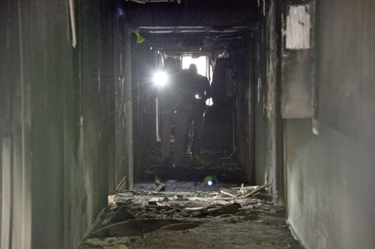 Investigators walk through an interior corridor after a fire at a three-story apartment complex early Saturday, Dec. 21, 2019 in Las Vegas. The fire was in first-floor unit of the Alpine Motel Apartments and its cause was under investigation, the department said. Authorities say multiple fatalities were reported and many more were injured.