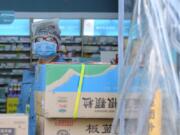 A clerk wearing a face mask and a plastic bag stands in a pharmacy in Wuhan in central China&#039;s Hubei Province, Friday, Jan. 31, 2020. The U.S. advised against all travel to China as the number of cases of a worrying new virus spiked more than tenfold in a week, including the highest death toll in a 24-hour period reported Friday.