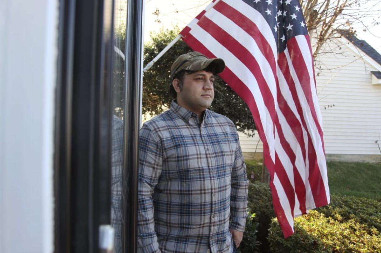 In this Monday, Dec. 16, 2019, photo, Zia Ghafoori stands beside an American flag hanging at his Charlotte, N.C., home. The Afghan interpreter spent 14 years working alongside U.S. Special Forces. He received a Special Immigrant Visa in 2014 and is working toward becoming a U.S. citizen.