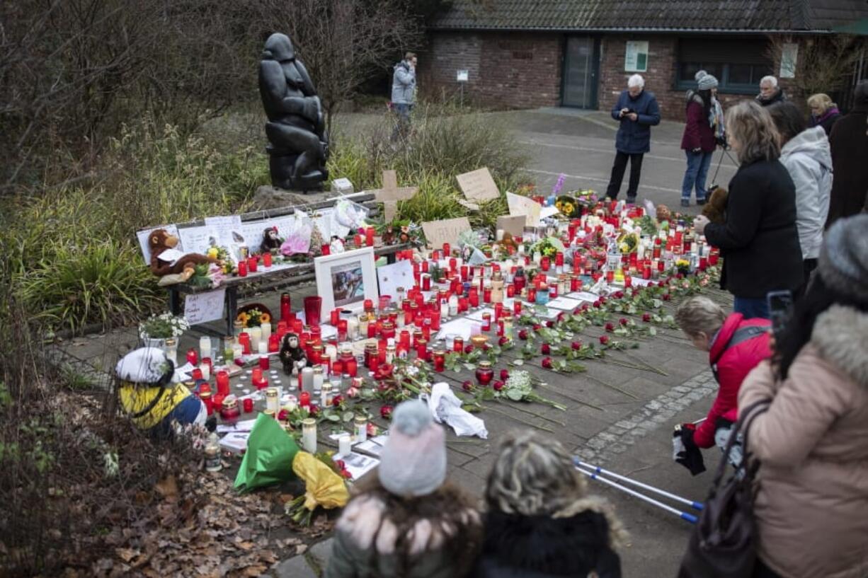 A women lights a candle at the main entrance of the Zoo in Krefeld, Germany, Thursday, Jan. 2, 2020. Three woman are under investigation for launching paper sky lanterns blamed for setting off a fire that destroyed an ape house at the zoo in the first few minutes of the new year, killing more than 30 animals, officials said Thursday.