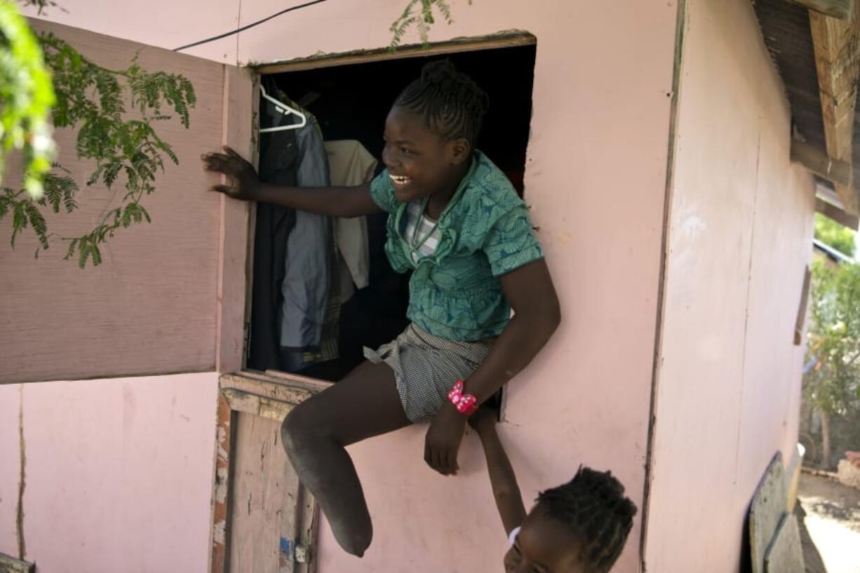 In this Jan. 3, 2020 photo, Rose-Berline Thomas sits in a window to speak with her mother outside at their home in Canaan, a district in Croix des Bouquets, Haiti, created for people who lost their homes in the earthquake 10 years ago. Rose-Berline Thomas was 2-years-old when the earthquake collapsed her family&#039;s home on top of her, crushing her foot.