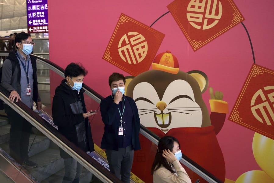 People wear face masks as they ride an escalator at the Hong Kong International Airport in Hong Kong, Tuesday, Jan. 21, 2020. Face masks sold out and temperature checks at airports and train stations became the new norm as China strove Tuesday to control the outbreak of a new coronavirus that has reached four other countries and territories and threatens to spread further during the Lunar New Year travel rush.