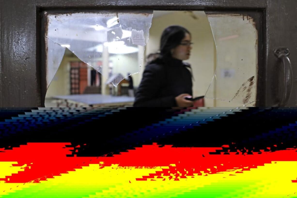 A student is seen through broken glass as she walks inside the hostel canteen room vandalized after Sunday&#039;s assault by masked assailants at the Jawaharlal Nehru University in New Delhi, India, Monday, Jan. 6, 2020. More than 20 people were injured in the attack opposition lawmakers are trying to link to the government.