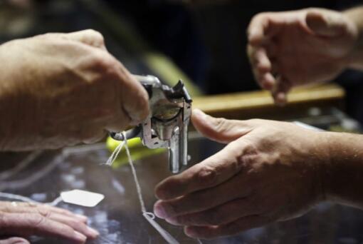 FILE - In this Oct. 20, 2017, file photo, a sales clerk hands a pistol, being sold on behalf of the Aberdeen Police Department, to a customer to look at before an auction at Johnny&#039;s Auction House, where the company handles gun sales for police departments and the Lewis County Sheriff&#039;s Office, in Rochester, Wash. After years of trying, the Washington state House of Representatives passed a bill Thursday, Jan. 23, 2020, that allows the State Patrol to destroy guns they confiscated during criminal investigations.