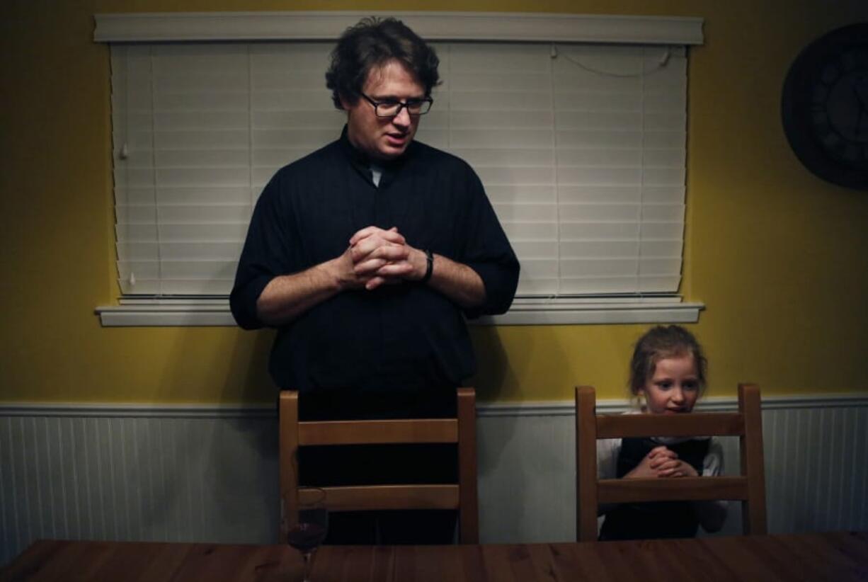 In this Feb. 7, 2020, photo, converted Catholic Priest Joshua Whitfield, left, his daughter Zoe-Catherine, 5, and the rest of his family stand behind their chairs to say grace before dinner in north Dallas.