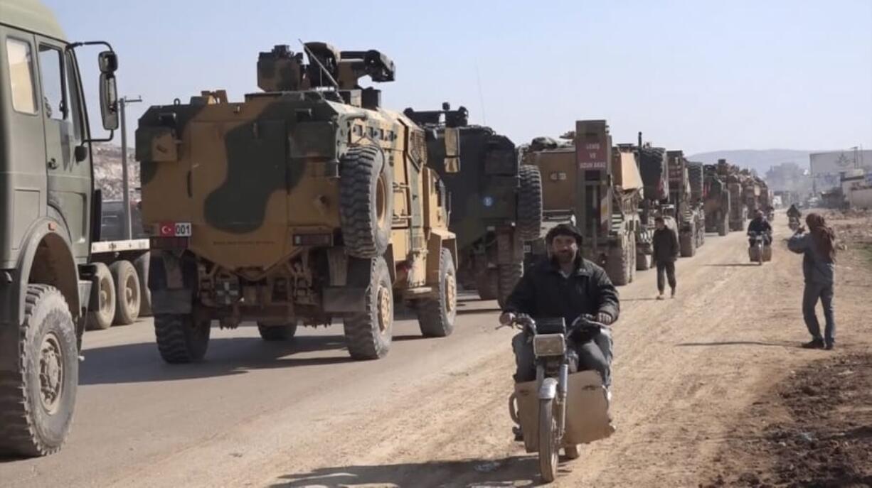 In this frame grab from video taken on Sunday, Feb. 2, 2020, people ride their motorcycles next to a Turkey Armed Forces convoy is seen at the northern town of Sarmada, in Idlib province, Syria. A large Turkish military convoy moved into the rebel-held areas of northwest Syria on Sunday, witnesses on the ground said, adding it appeared to be heading towards the south of Idlib province.