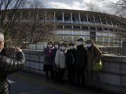 Tourists wear masks as they pause for photos with the New National Stadium, a venue for the opening and closing ceremonies at the Tokyo 2020 Olympics, Sunday, Feb. 23, 2020, in Tokyo. (AP Photo/Jae C.