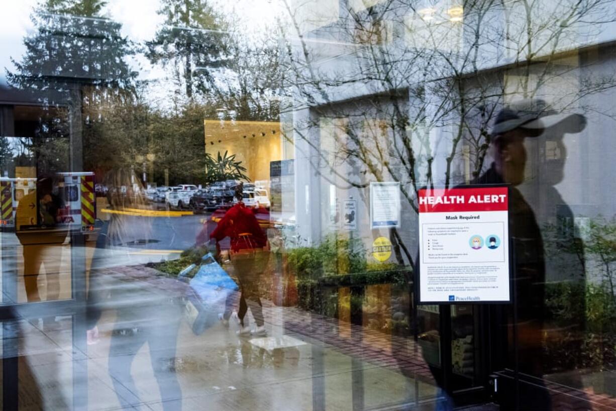 Visitors walk past a health alert sign with measures meant to prevent the spread of coronavirus at an entrance to PeaceHealth Southwest Medical Center in Vancouver. The hospital is implementing some protocols to help protect against the spread of COVID-19.