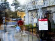 Visitors walk past a health alert sign with measures meant to prevent the spread of coronavirus at an entrance to PeaceHealth Southwest Medical Center in Vancouver. The hospital is implementing some protocols to help protect against the spread of COVID-19.