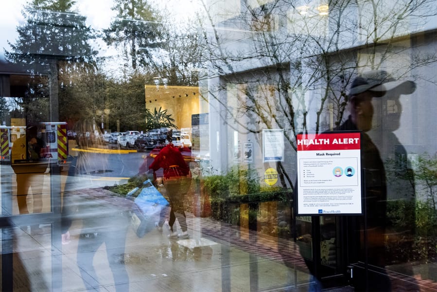 Visitors walk past a health alert sign with measures meant to prevent the spread of coronavirus at an entrance to PeaceHealth Southwest Medical Center in Vancouver. The hospital is implementing some protocols to help protect against the spread of COVID-19.