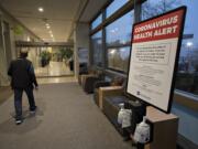 A man walks past a coronavirus health alert posted at one of the entrances to the Firstenburg Tower at PeaceHealth Southwest Medical Center on Monday morning.