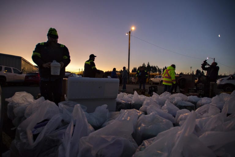 Michael Vestal, a mechanic with Evergreen School District, left, adds ice to boxes of milk near Burton Elementary School as the sun rises before drivers pick them up to be distributed to local students on Tuesday morning, March 17, 2020.