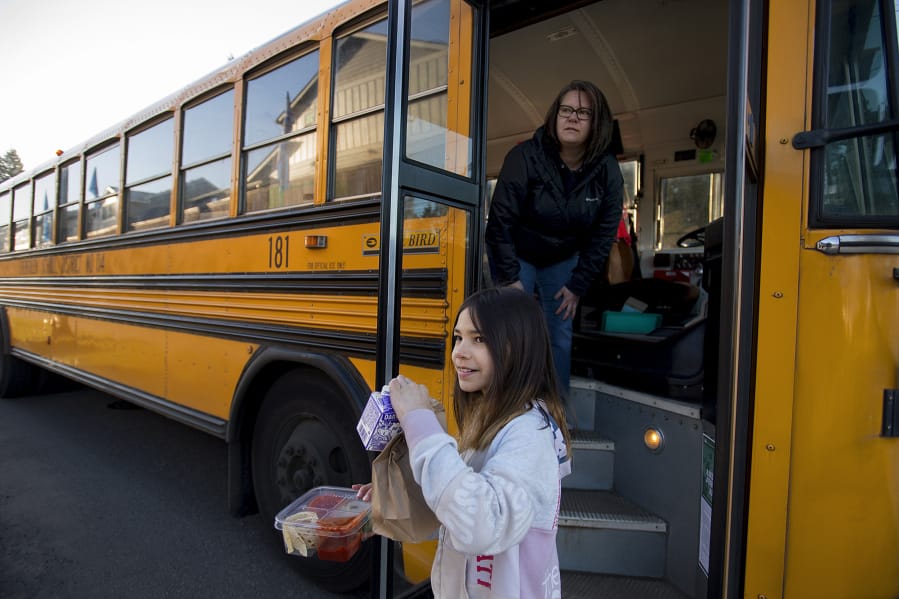 Kamryn Tanioka, 9, foreground, picks up her breakfast and lunch from school bus driver Tanisha Cardiel as she makes deliveries for students on her route in east Vancouver on March 17, 2020.