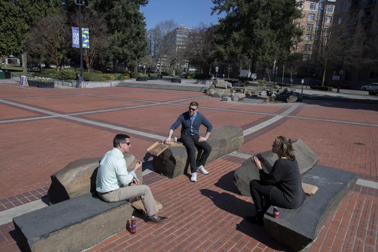 Mike True, from left, of Vancouver, Jordan Boldt of Vancouver and Kim Newman of Camas give each other space as they gather to enjoy takeout from Nonavo Pizza on their lunch break in a nearly empty Esther Short Park on Thursday. Boldt said the sunny weather was a good excuse to get outside. &quot;You gotta make the best of it,&quot; he said about the COVID-19 situation.